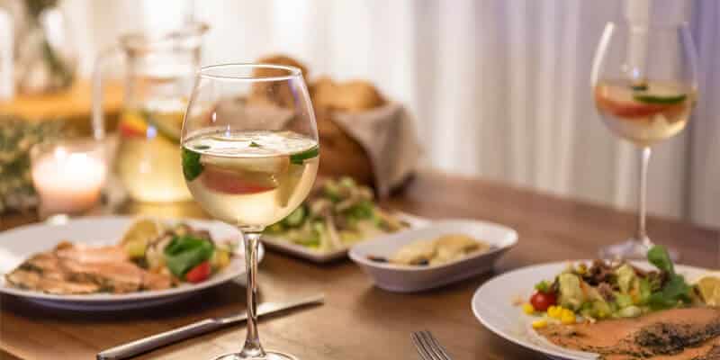 A table with 2 plates of food, and 2 glasses of wine on it